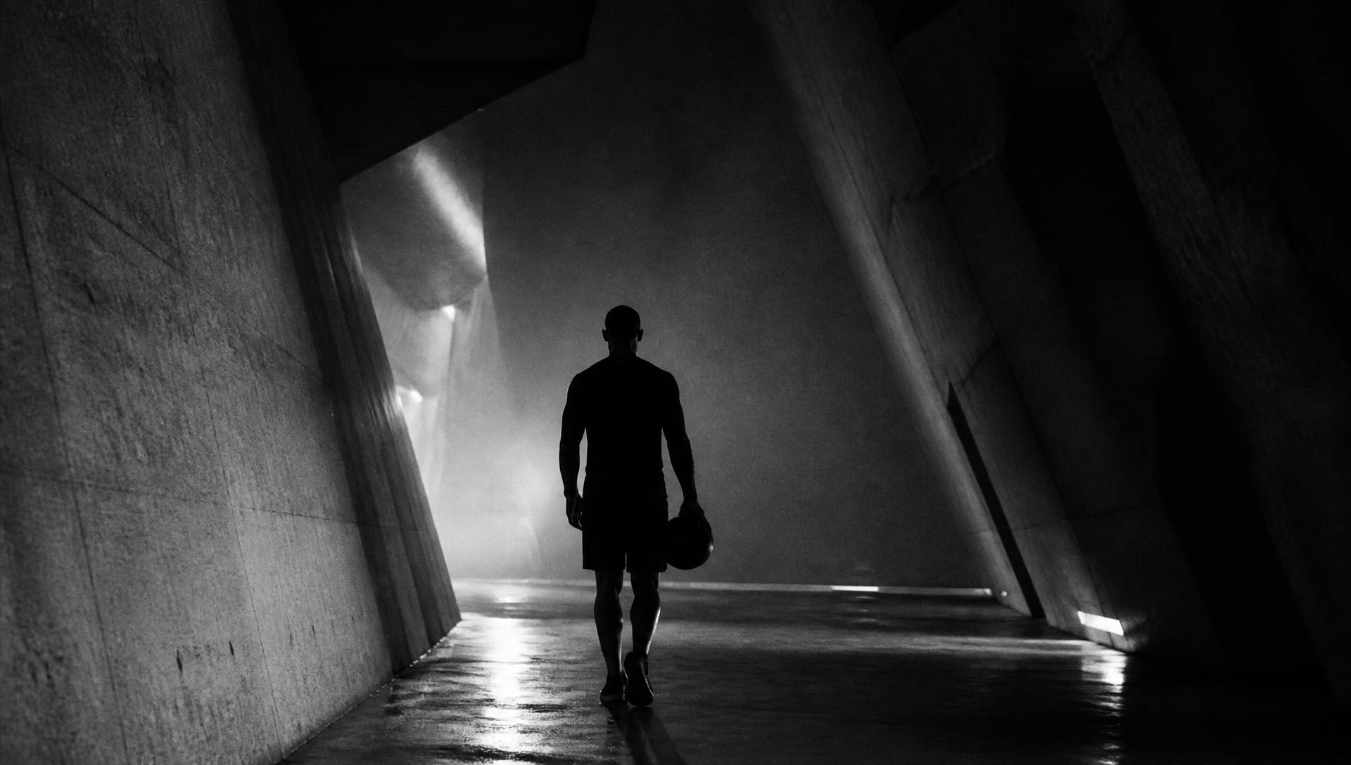 A lone athlete walking through dark concrete architecture